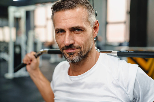 Attractive confident healthy sports man using seated lat pulldown machine in the gym, close up - Fotó, kép