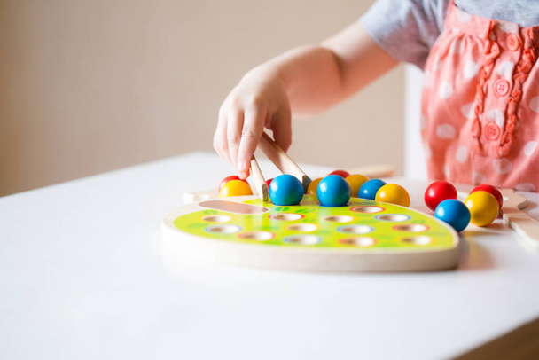 small baby lays out balls with tweezers in holes . concept of fine motor skills development, teaching preschool children. - Фото, изображение