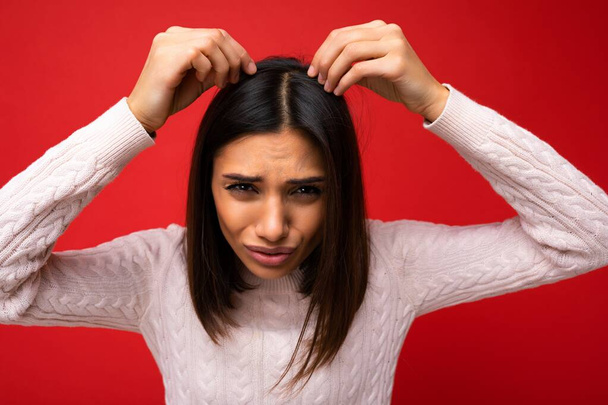 Portrait of beautiful dissatisfied sad young brunette woman wearing knitted jersey isolated over red background with free space and touching short hair and having problems - Photo, Image