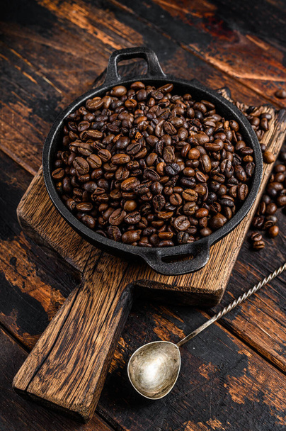 Dark roasted Coffee beans in a pan. Dark wooden background. Top view - Photo, Image