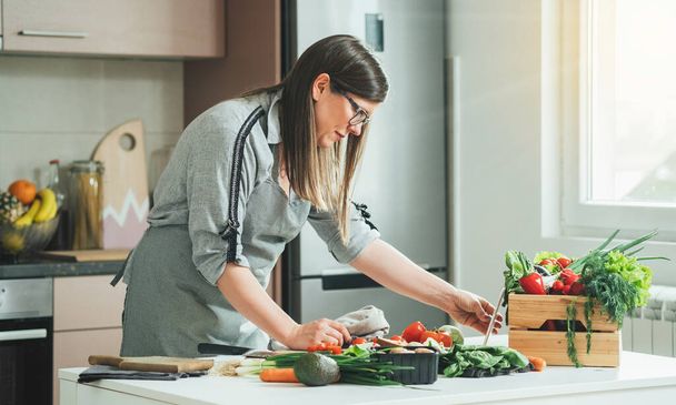 Όμορφη γυναίκα βλέποντας συνταγή για να προετοιμάσει τα τρόφιμα στη σύγχρονη κουζίνα.Χαρούμενη γυναίκα διαβάζοντας online συνταγή για το ψηφιακό δισκίο, ενώ το μαγείρεμα γεύμα στην κουζίνα στο σπίτι - Φωτογραφία, εικόνα