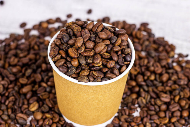 Καφέ χάρτινο κύπελλο μιας χρήσης με καφέ και καβουρδισμένους κόκκους καφέ στο τραπέζι με αντίγραφο χώρου στο φως φόντο. Takeaway έννοια των τροφίμων. - Φωτογραφία, εικόνα