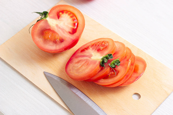 キッチンの木製のまな板にナイフでカット明るい新鮮な生の赤いトマトは、光の背景に. - 写真・画像