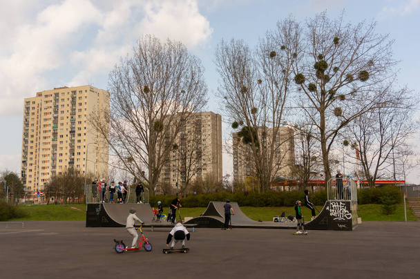 POZNAN, POLAND - Apr 18, 2021: Children having fun with skates on a park with apartment buildings in the background. - Zdjęcie, obraz