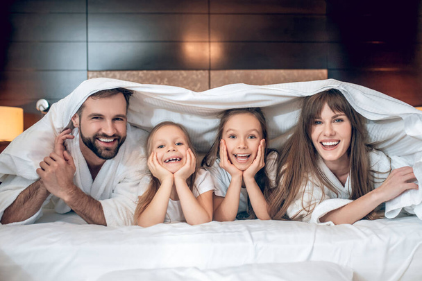 Smiling family in white robes lying in bed and having fun - Photo, image