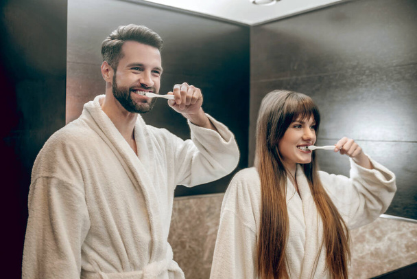 Young couple in bath robes brushing teeth together - Фото, зображення
