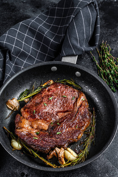 Roasted rib eye steak, ribeye beef meat in a pan. Black background. Top view - Valokuva, kuva