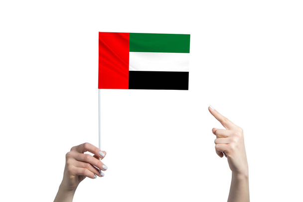 A beautiful female hand holds a United Arab Emirates flag to which she shows the finger of her other hand, isolated on white background. - Photo, Image