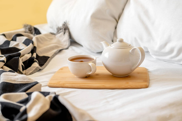 Tray of tea on bed. White bedding sheets with blanket and pillow. Breakfast in bed. Warm and cosy scandinavian hygge concept - cup of tea. - Foto, Bild