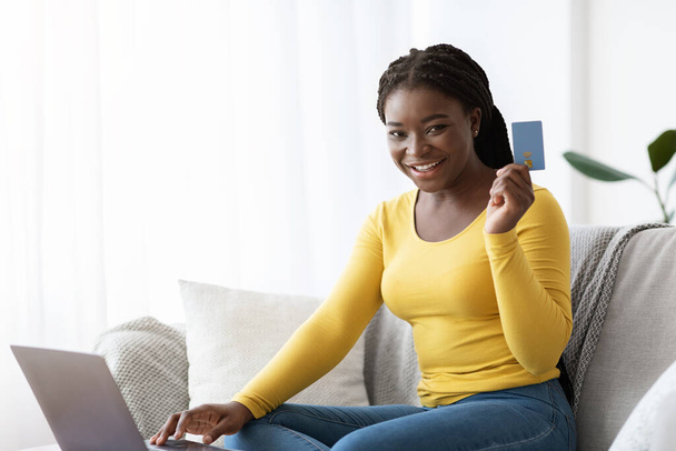 Online nakupování. Šťastná africká dáma s kreditní kartou a notebookem doma - Fotografie, Obrázek
