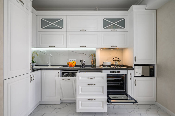 Luxueux intérieur de cuisine moderne blanche, tiroirs retirés, porte lave-vaisselle ouverte - Photo, image