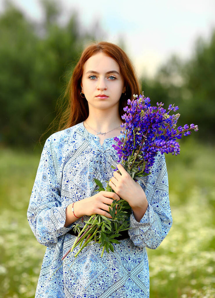 Portrait with a young girl, holding a bouquet of lilac lupins in her hands. Stunning sky and sunset background. Nature. Summer concept.  - Photo, image