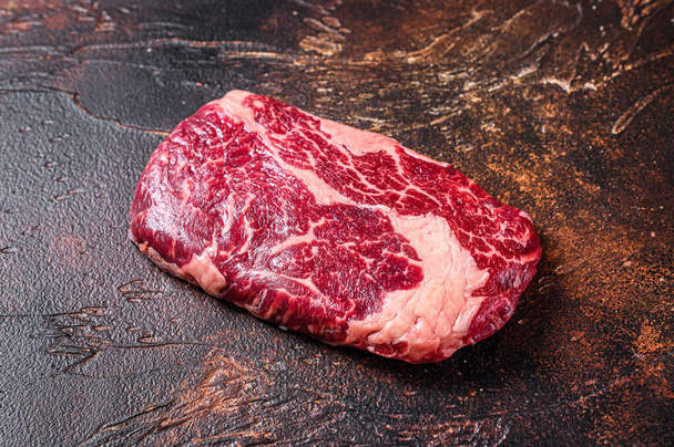 Сырой стейк из говяжьего мяса на мясном столе, приготовленный для приготовления пищи. Темный фон. Вид сверху - Фото, изображение