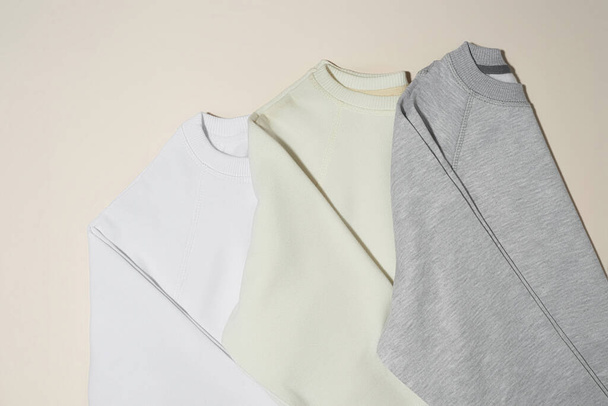 Closeup of folded gray, white and ivory sport blank sweatshirts isolated on pale beige background - Fotó, kép