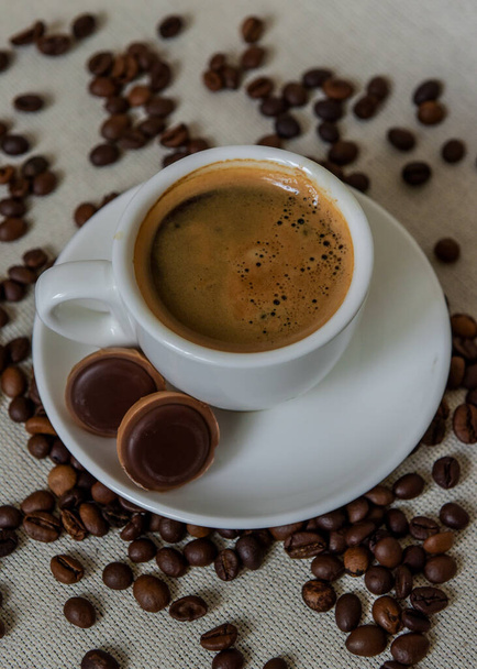 Uma xícara de café forte. Copo de cerâmica branca com café em um pires. Close-up. Grãos de café. Café da manhã - Foto, Imagem
