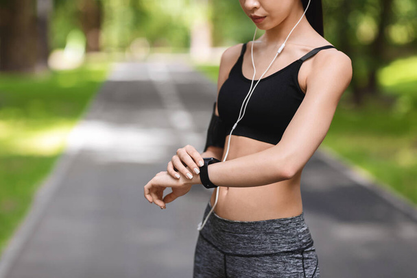 Unrecognizable sporty woman setting up fitness smartwatch before running in park - Photo, Image