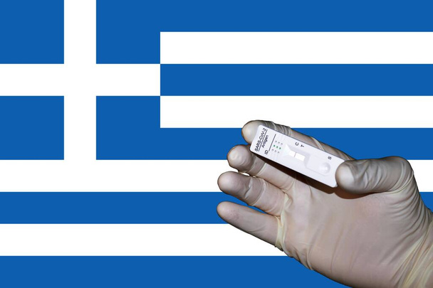 Ένα χέρι που δείχνει ένα αρνητικό αντιγονικό κορόνα ταχεία δοκιμή μπροστά από μια σημαία της Ελλάδας - Φωτογραφία, εικόνα