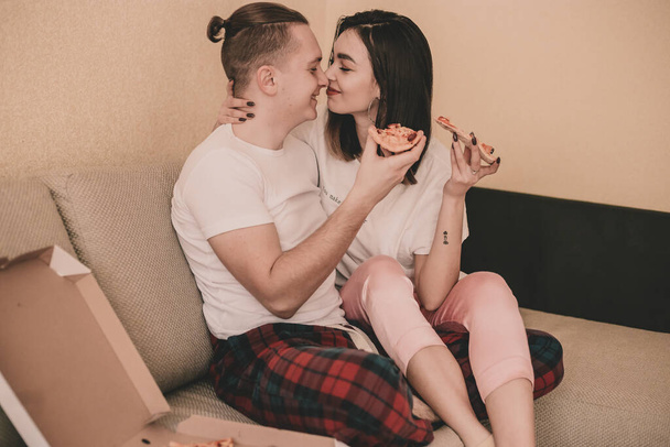 Пара в домашньому одязі вдома на ліжку їсть піцу
 - Фото, зображення