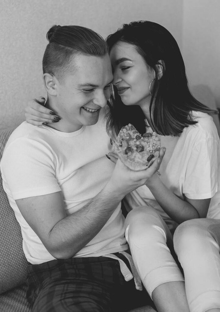 Couple in home clothes at home on bed eating pizza black and white photo - Zdjęcie, obraz