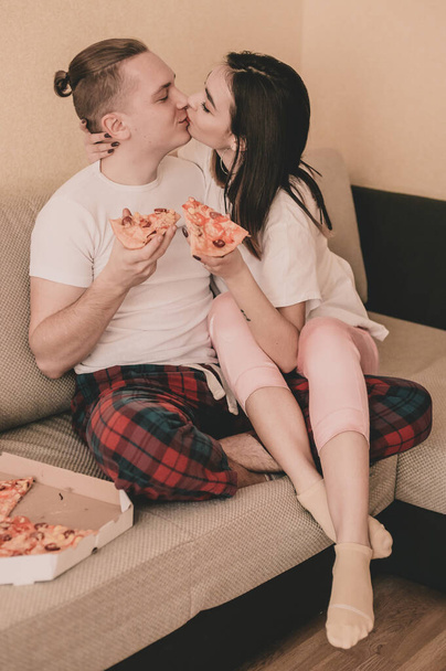 Couple in home clothes at home on bed eating pizza - Фото, изображение
