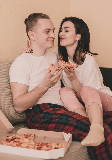 Couple en vêtements à la maison à la maison sur le lit manger de la pizza - Photo, image