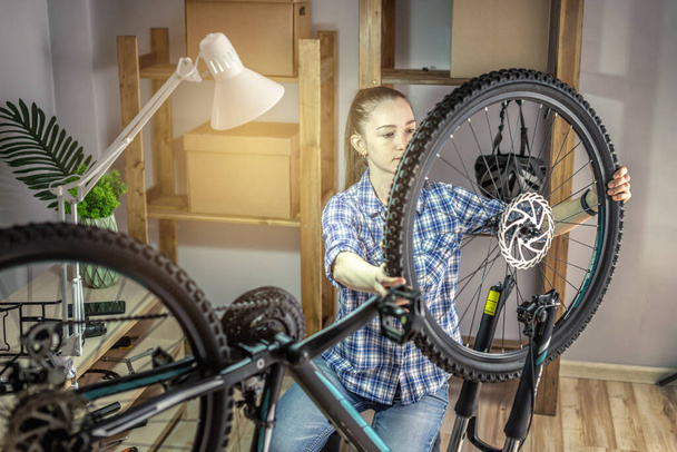 Женщина в мастерской разбирает его велосипед и чинит его. Концепция технического обслуживания и подготовки к новому сезону - Фото, изображение