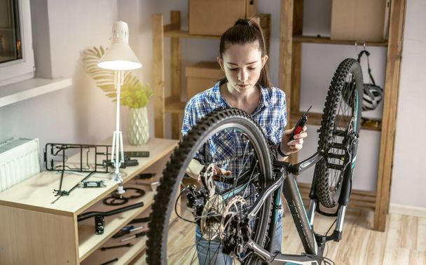 Una mujer está realizando mantenimiento en su bicicleta de montaña. Concepto de fijación y preparación de la bicicleta para la nueva temporada - Foto, Imagen