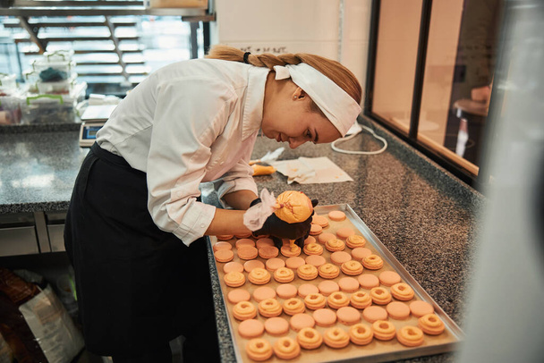 Focused pastry chef putting icing on custom-made macarons - Foto, Imagen