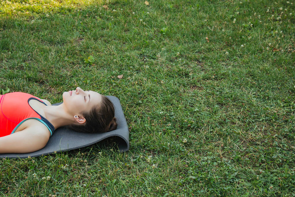 Chica europea en un chándal ligero haciendo yoga en el parque por la tarde en el verano. Gimnasia en la naturaleza. Mujer delgada al aire libre. - Foto, imagen