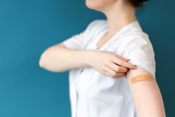 コロナウイルスワクチン。看護師はそれに固執したバンドエイドで手を示しています。接近中だ。濃い青の背景。予防接種とウイルス対策の概念. - 写真・画像