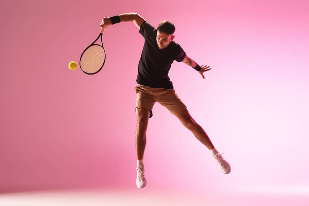 Young caucasian man playing tennis isolated on pink studio background, action and motion concept - Foto, Imagem