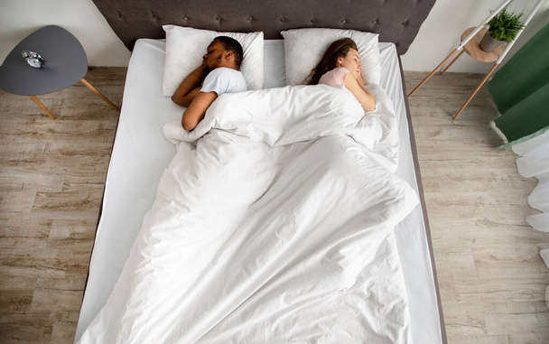 Vista superior de la joven pareja interracial durmiendo espalda con espalda en la cama en casa. Concepto de ruptura familiar o divorcio - Foto, imagen