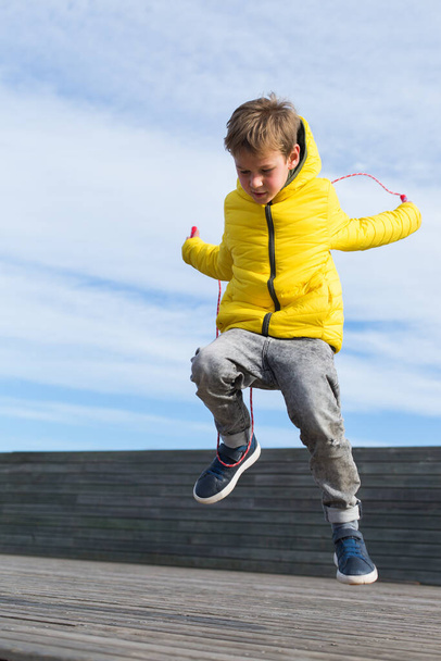Stylish young boy, teenager is jumping with skipping rope, outdoors - Foto, imagen