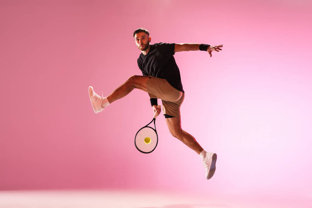 Young caucasian man playing tennis isolated on pink studio background, action and motion concept - Fotografie, Obrázek