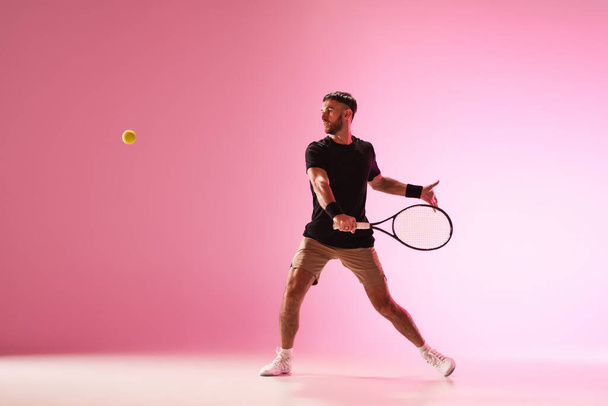 Mladý běloch hraje tenis izolovaný na růžovém pozadí studia, akční a pohybový koncept - Fotografie, Obrázek