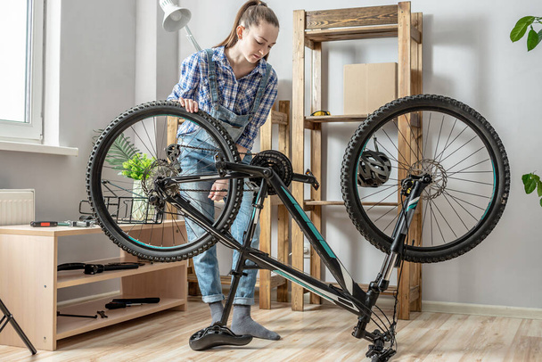 Una mujer está realizando mantenimiento en su bicicleta de montaña. Concepto de fijación y preparación de la bicicleta para la nueva temporada - Foto, Imagen