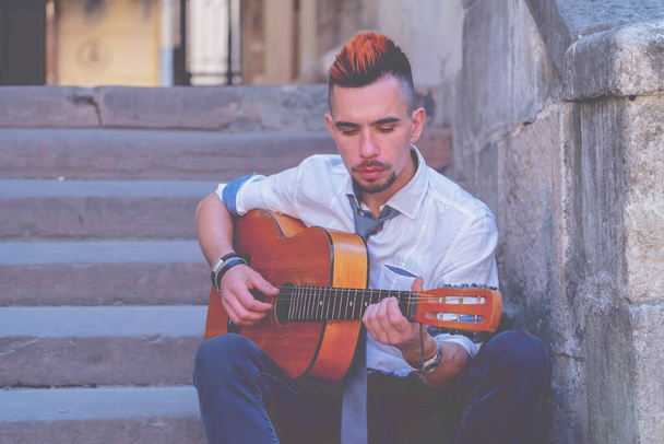 Young man playing the guitar outdoors in old European city. Horizontal image.  - Photo, Image