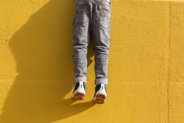 Ноги молодого хлопчика в сірих джинсах на жовтій стіні
 - Фото, зображення