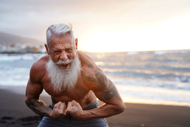 Fit and muscular senior man exercising on the beach. In a healthy body, healthy mind. Age is just a number. People on retirement. - Fotografie, Obrázek