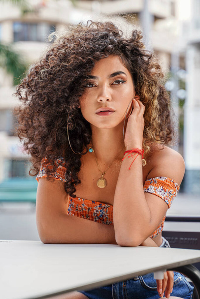 Retrato de belleza de mujer colombiana atractiva con peinado afro y maquillaje delicado posando al aire libre, mirando a la cámara. - Foto, imagen
