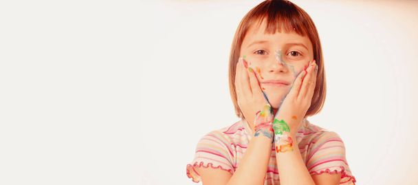 Η ομορφιά και η τέχνη. Μικρό όμορφο κορίτσι με πολύχρωμο μακιγιάζ για παιδιά που δείχνει ζωγραφισμένα χέρια. Ελεύθερος χώρος αντιγραφής για σχεδιασμό. - Φωτογραφία, εικόνα