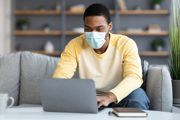 Homem de negócios preto em máscara protetora usando laptop em casa - Foto, Imagem