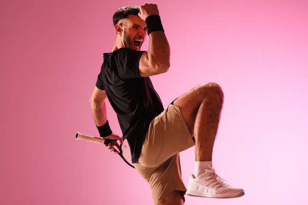 Young caucasian man playing tennis isolated on pink studio background, action and motion concept - Фото, изображение