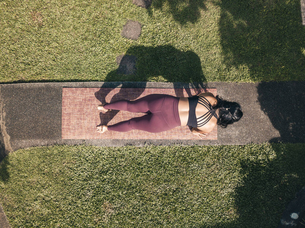Κάτοψη μιας γυναίκας που κάνει ασκήσεις τεντώματος για να προετοιμαστεί για μια συνεδρία γιόγκα. Σε ένα μονοπάτι σε ένα πάρκο ή κήπο ενός σπιτιού. - Φωτογραφία, εικόνα