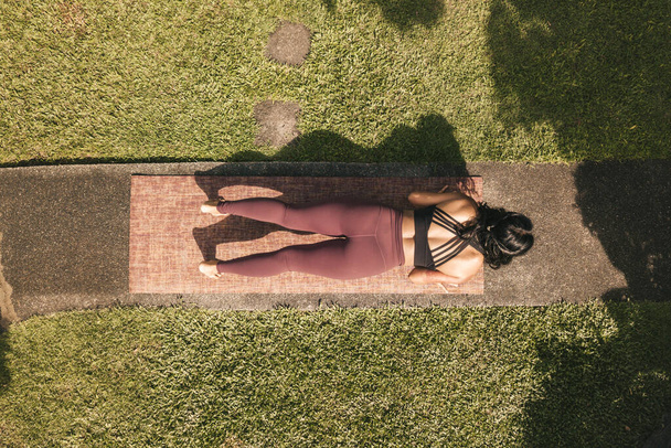 Vista superior de una mujer haciendo flexiones o preparándose para hacer una pose de cobra o Bhujangasana. Sesión de yoga en un sendero en un parque o jardín de una casa. - Foto, imagen