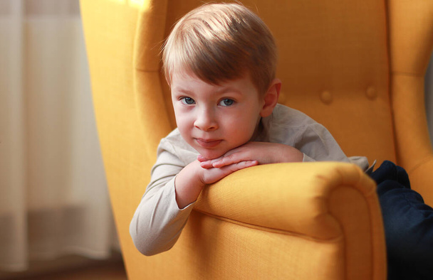 Маленький блондин на жовтому кріслі. Міжнародний день дітей. - Фото, зображення