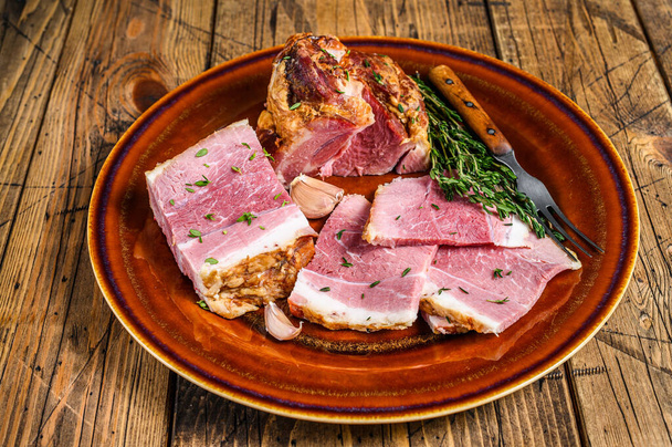 Geräuchertes Schweinefleisch und Speckscheiben auf einem rustikalen Teller. Holzuntergrund. Ansicht von oben - Foto, Bild