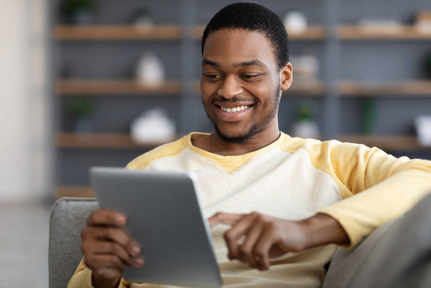 Positivo uomo nero sdraiato sul divano, utilizzando tablet digitale, primo piano - Foto, immagini