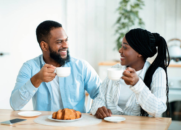Pozytywne młodych czarnych małżonków korzystających rano kawy i rogaliki w kuchni - Zdjęcie, obraz