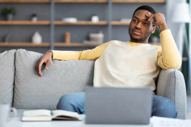 Pensive černý podnikatel sedí na gauči před notebookem - Fotografie, Obrázek